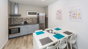 A compact kitchen with modern appliances, a dining area with a white table and chairs, and artwork on the walls. - Rooms and Apartments Bruno (Split)