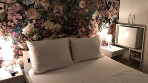 A bedroom with a floral wallpaper, a bed with white bedding, a bedside table with a lamp, and a TV on a stand. - Rooms and Apartments Bruno (Split)