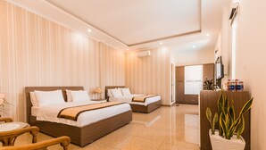 A hotel room with two beds, a wooden chair, a small table, a potted plant, and a minibar. - Marina Luxury Vung Tau (Ho Chi Minh City)