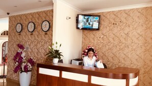 A reception desk with a wooden finish, a potted plant, and a wall-mounted television. - Marina Luxury Vung Tau (Ho Chi Minh City)