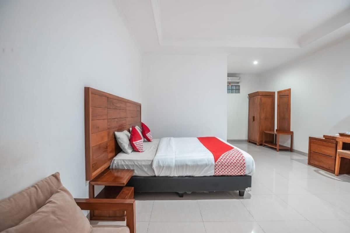 A bedroom with a wooden headboard, a bed with white bedding and red accents, a wooden nightstand, a chair, and a wardrobe.