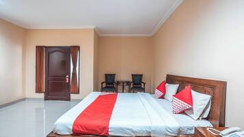 A hotel room with a bed, a bedside table with a phone, a small table with chairs, and a door with curtains.