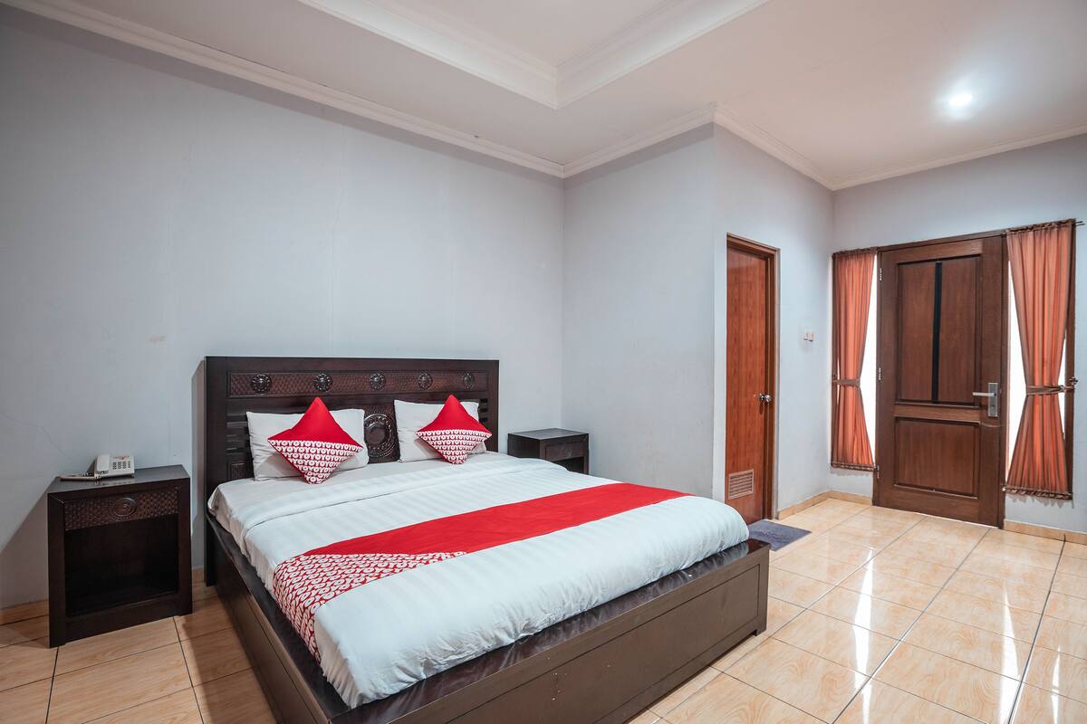 A bedroom with a large bed, two bedside tables, a wooden wardrobe, and a door with curtains.