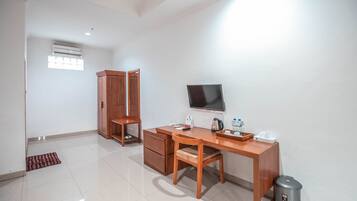A room with a wooden desk, chair, and wardrobe. There is a television mounted on the wall and a trash bin near the desk.