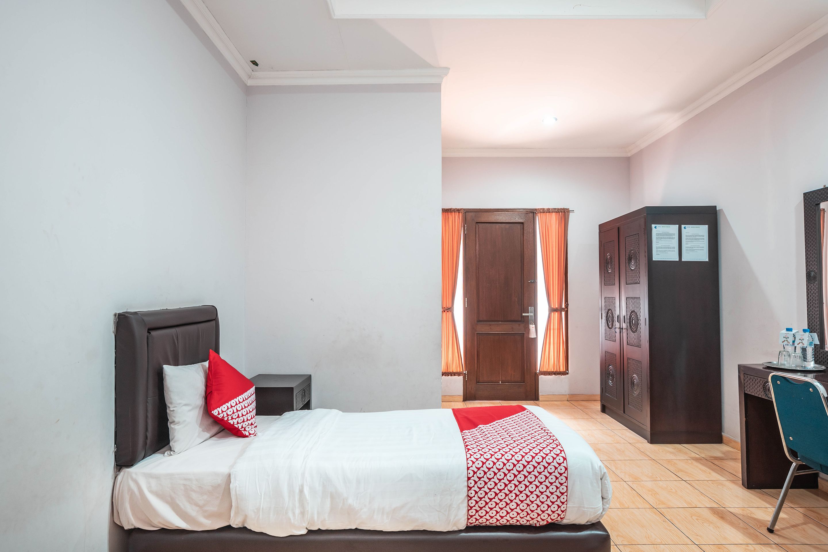 A hotel room with a bed, a desk, a wardrobe, and a door with curtains.
