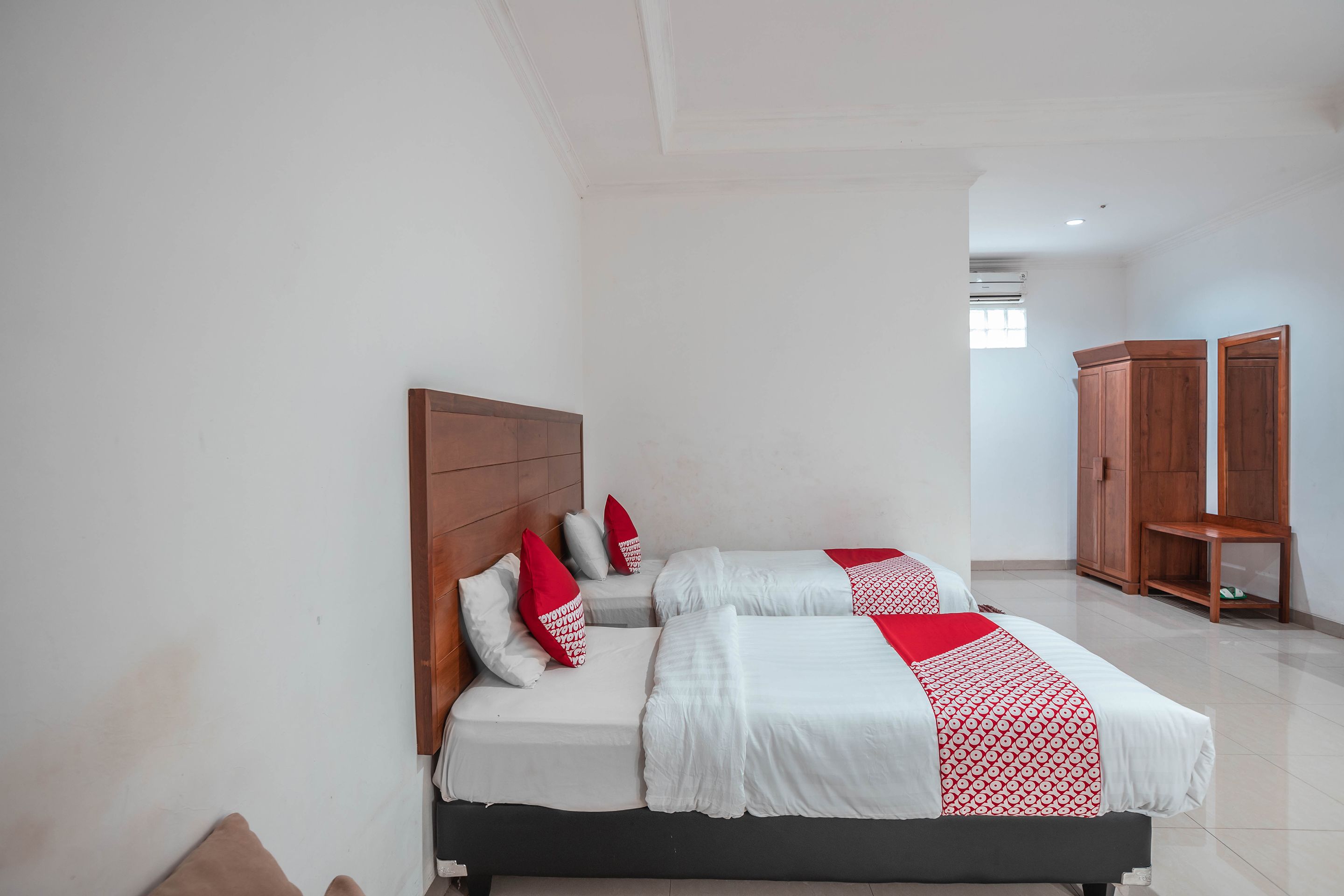 A hotel room with two beds, a wooden wardrobe, and a small table.