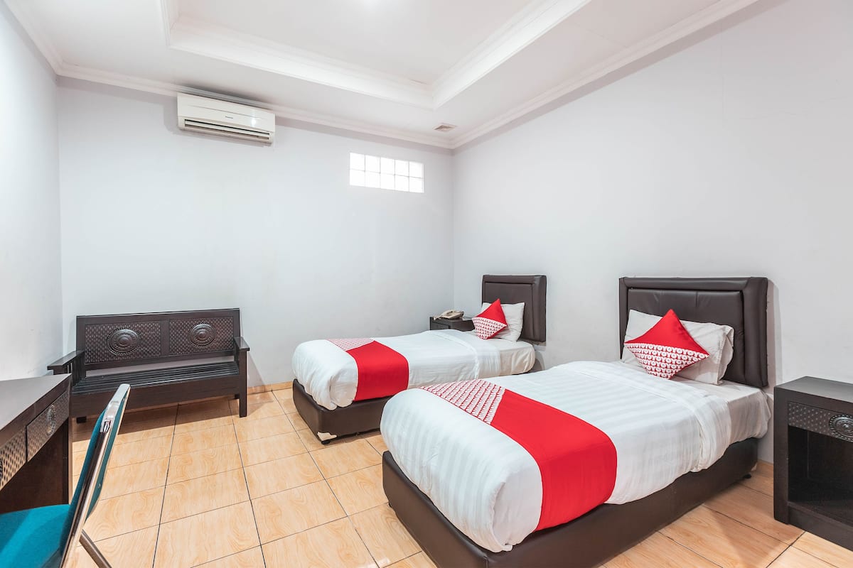 A hotel room with two beds, a desk, a chair, and a window.