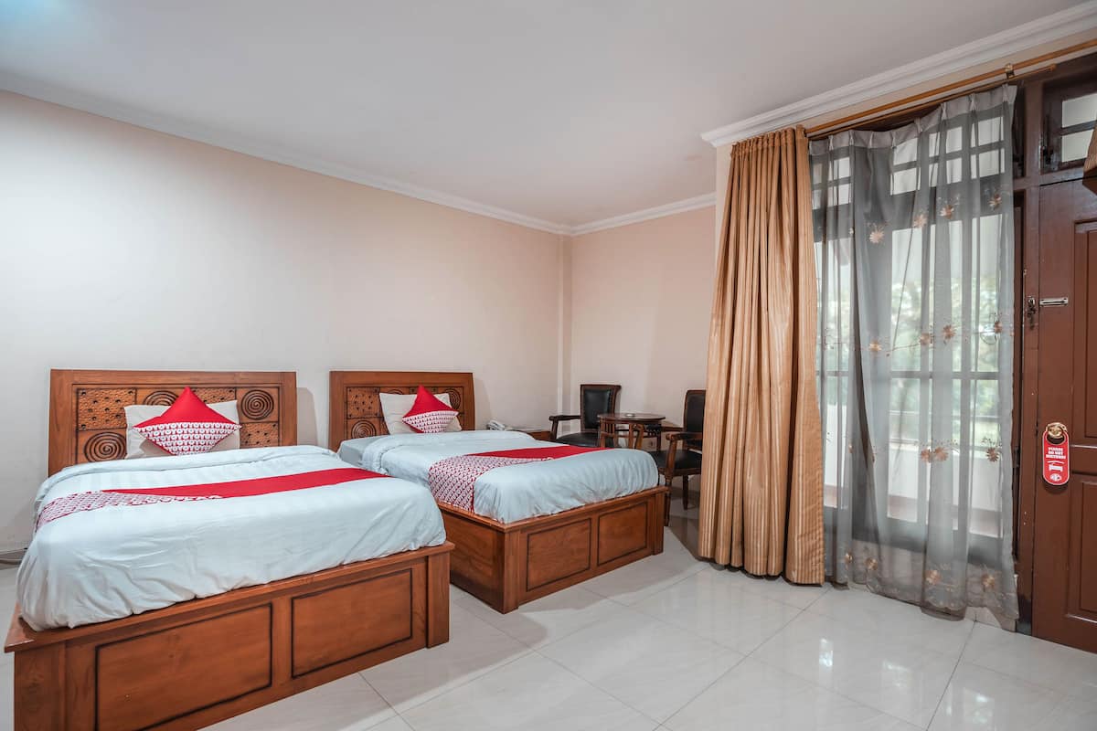 A hotel room with two wooden beds, a desk, and a wardrobe.