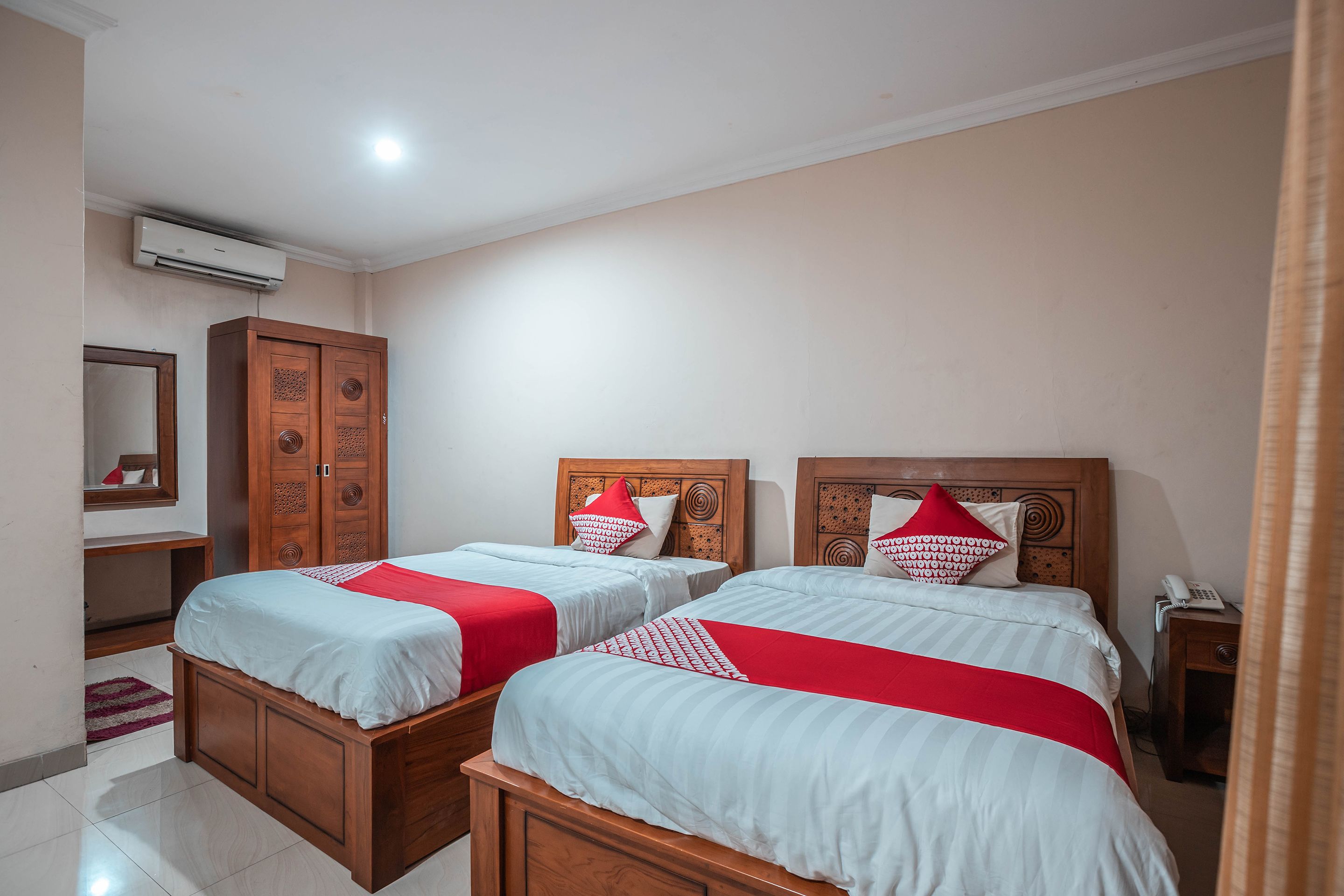 Een hotelkamer met twee bedden, een houten garderobe, een spiegel en een telefoon op een nachtkastje.