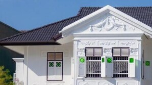 A two-story colonial-style building with a symmetrical facade, featuring a central entrance with a decorative archway and a balcony with a railing. - Sound Gallery House - Hostel (Phuket)