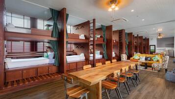 A multi-level bunk bed room with wooden furniture, a dining table with chairs, and a sofa in a modern interior.
