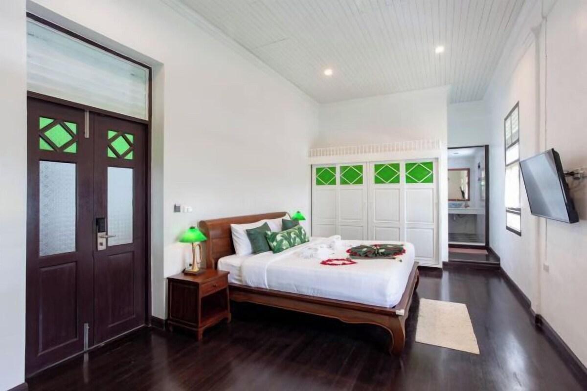 Un dormitorio con cama de madera, mesita de noche, lámpara y televisor montado en la pared.