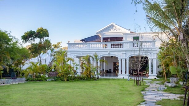 A white colonial-style building with a central courtyard, surrounded by lush greenery and palm trees. - Sound Gallery House - Hostel (Phuket)