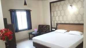 A bedroom with a large bed, a bedside table, a lamp, a window with curtains, and a vase with flowers. - Hotel PP Palace (Puri)