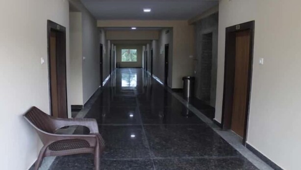 A long, narrow hallway with a shiny black floor, a chair on the left, and doors on both sides. - Hotel PP Palace (Puri)