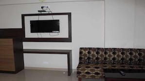 A living room with a flat-screen TV mounted on the wall, a wooden console table, and a patterned sofa. - Hotel PP Palace (Puri)