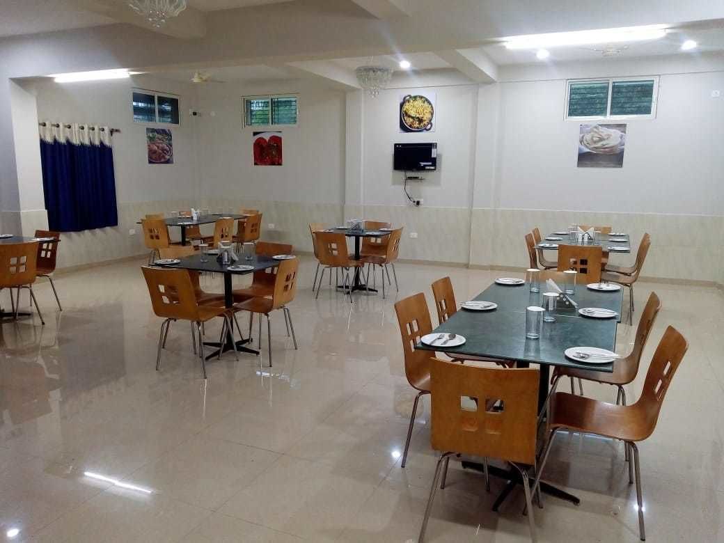 A dining area with multiple tables and chairs, a flat-screen TV mounted on the wall, and a chandelier.