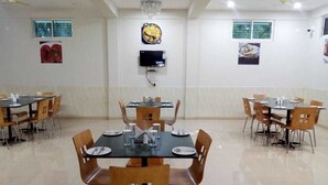 A dining area with multiple tables and chairs, a flat-screen TV mounted on the wall, and a ceiling fan. - Hotel PP Palace (Puri)