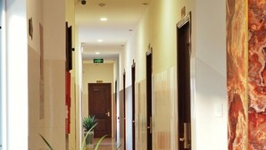 A hotel corridor with a marble wall, potted plants, and doors leading to rooms.