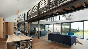 A spacious living area with a wooden dining table, a sofa, and a staircase leading to an upper level. - Villa with pool, ocean view (Batz-sur-Mer)