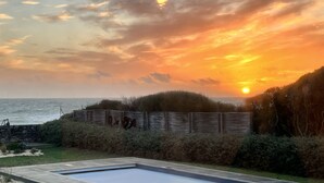 A sunset over a beach with a wooden fence and a swimming pool in the foreground. - Villa with pool, ocean view (Batz-sur-Mer)