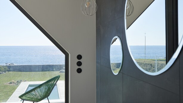 A modern interior with a large window overlooking the sea, a green chair, and a unique circular mirror. - Villa with pool, ocean view (Batz-sur-Mer)