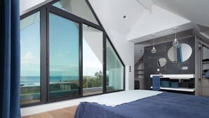 A modern bedroom with a large sliding glass door leading to a balcony with a view of the sea. - Villa with pool, ocean view (Batz-sur-Mer)