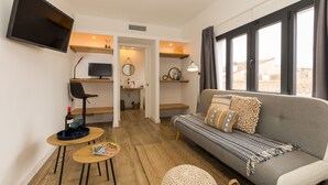 A compact living space with a sofa, a TV, a small table, and a chair. - Pardela Menorca Hotel (Es Castell)
