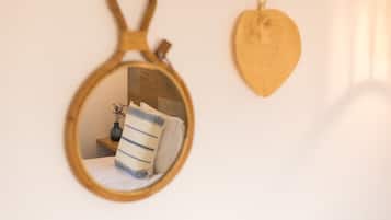 A round mirror with a wooden frame reflecting a bed with striped pillows and a vase of flowers.