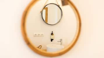 A bathroom with a round mirror, a white sink, and a bottle of hand soap on the wall.