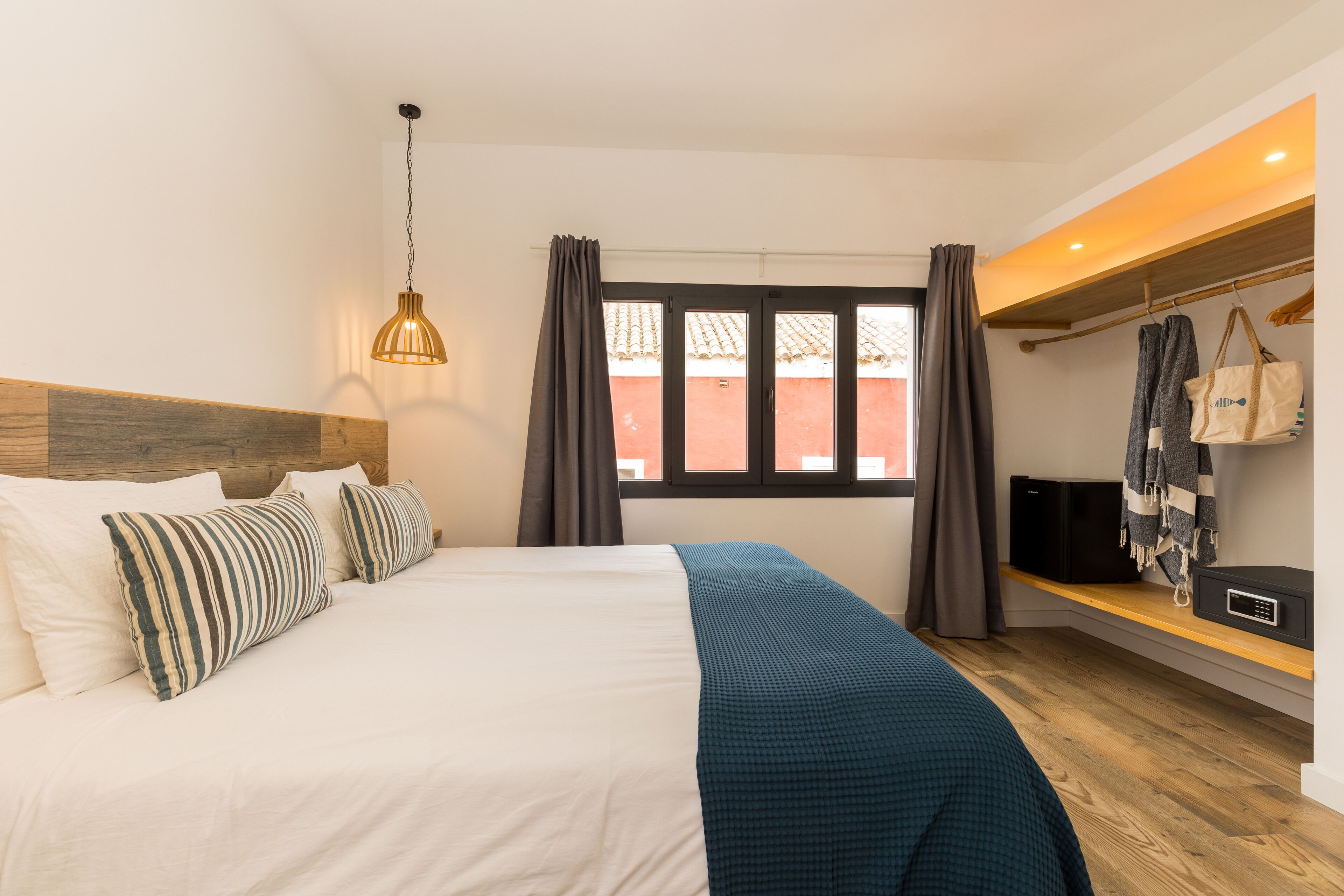 A neatly made bed with striped pillows, a blue blanket, and a hanging pendant light.