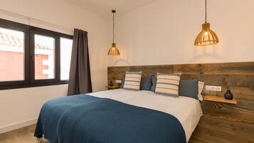 A bedroom with a bed, wooden headboard, two pendant lights, a nightstand, and a window with curtains.