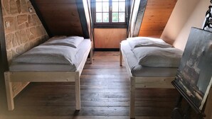 Un pequeño dormitorio en el ático con dos camas de madera, una pared de piedra y una ventana con vistas al verdor.