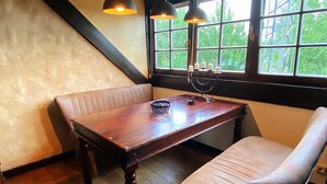 Un rincón acogedor con una mesa de madera y dos bancos acolchados, un candelabro y una ventana con vistas a follaje.