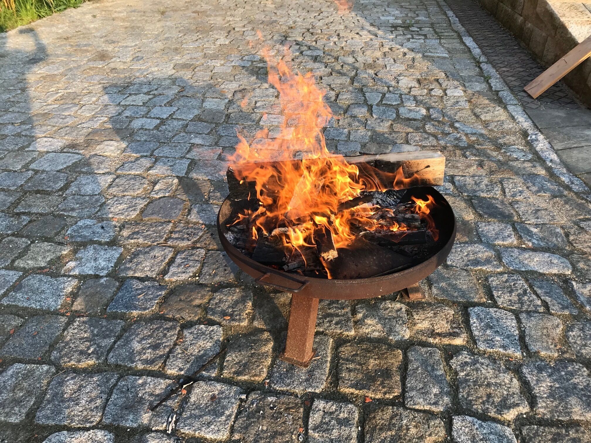 Metallinen nuotiopaikka, jossa palaa puuta, ja sen alla on mukulakivipäällyste.