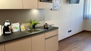 Une cuisine moderne avec un plan de travail noir, des armoires de couleur beige, un évier, une bouilloire, un livre et une petite plante.