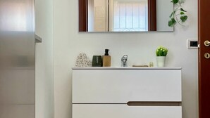 Un meuble-lavabo blanc pour la salle de bain, avec un miroir au-dessus, une petite plante en pot et quelques articles de toilette posés sur le plan.