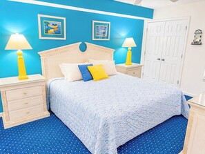 Un dormitorio con una cama, dos mesitas de noche, una lámpara de noche, una puerta y dos lámparas fijadas a la pared.