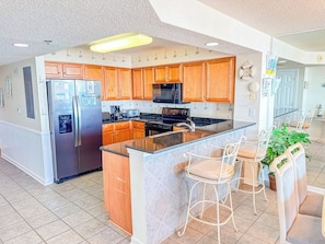 A modern kitchen with wooden cabinets, stainless steel appliances, and a central island with bar stools. - Crescent Shores S 210 (North Myrtle Beach)