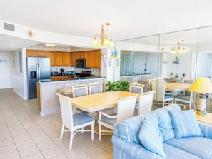 A modern kitchen with wooden cabinets, a central island, and a dining area with white chairs.