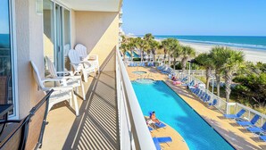 Un balcon avec des chaises blanches, une piscine et une vue sur la plage.