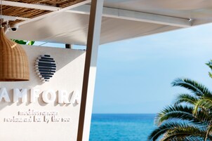 Señal del restaurante AMFORA Mediterráneo frente al mar, con vista al océano y palmeras.
