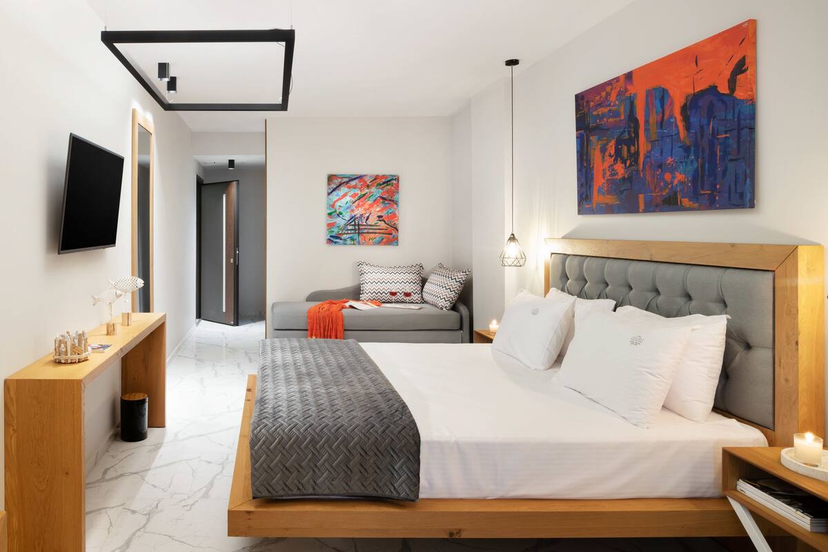 Un dormitorio moderno con una cama grande, un sofá, un televisor y obras de arte en las paredes.