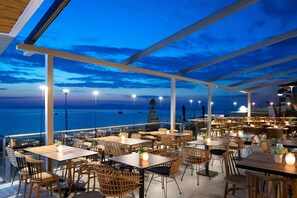 Un área de comedor al aire libre con mesas y sillas, con vista al mar.