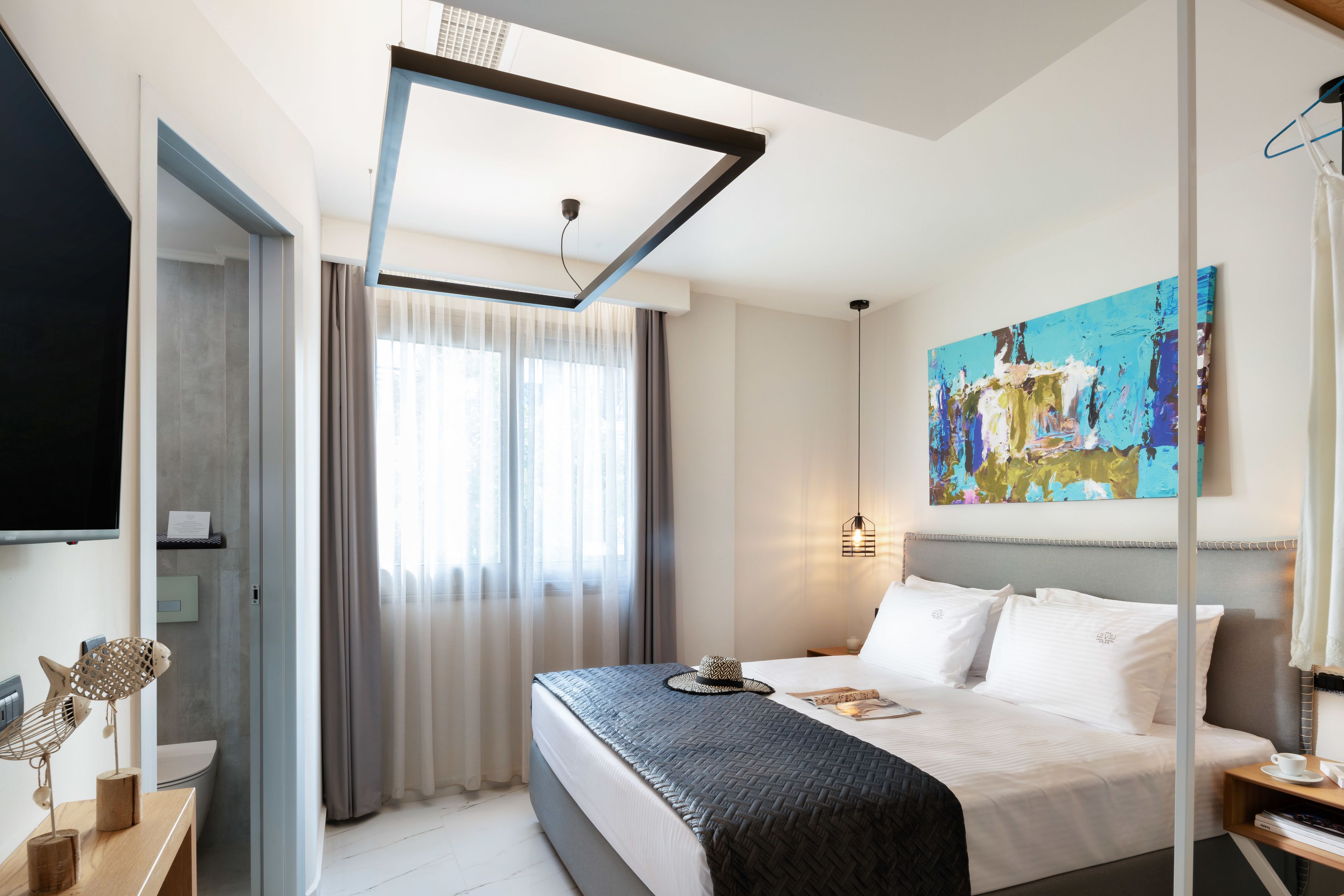 Habitación de hotel moderna con una cama grande, un televisor de pantalla plana, un cuadro y un escritorio con lámpara.
