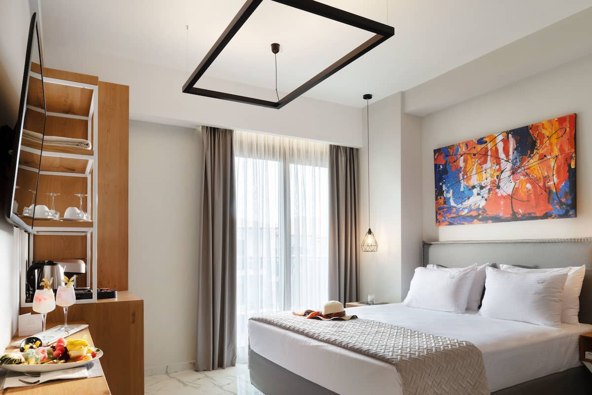Habitación de hotel moderna con una cama grande, un televisor de pantalla plana, un estante de madera con vasos y un cuadro en la pared.