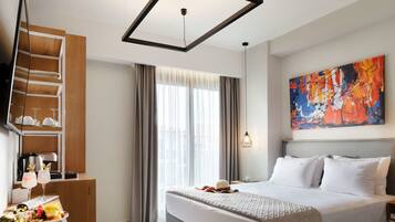 A modern hotel room with a large bed, a flat-screen TV, a wooden shelf with glasses, and a painting on the wall.