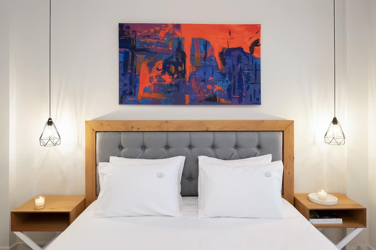 Un dormitorio moderno con cabecera capitonada, ropa de cama blanca y un cuadro abstracto grande sobre la cama.