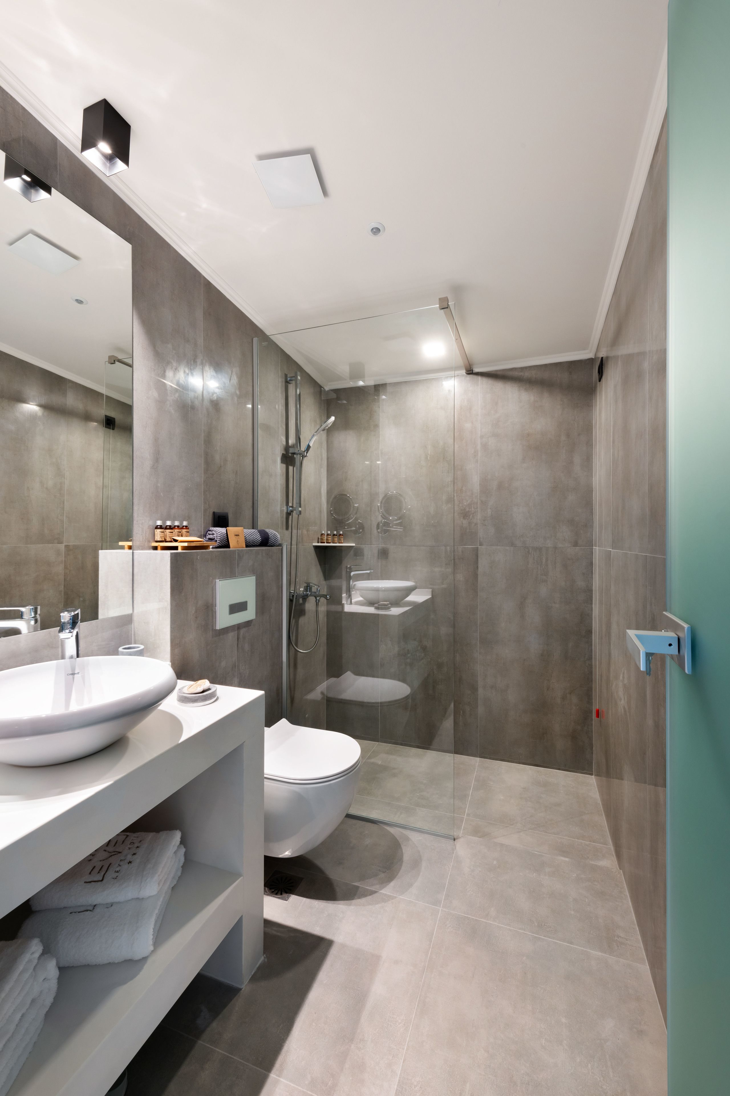 A modern bathroom with a large mirror, two sinks, a toilet, and a shower area.