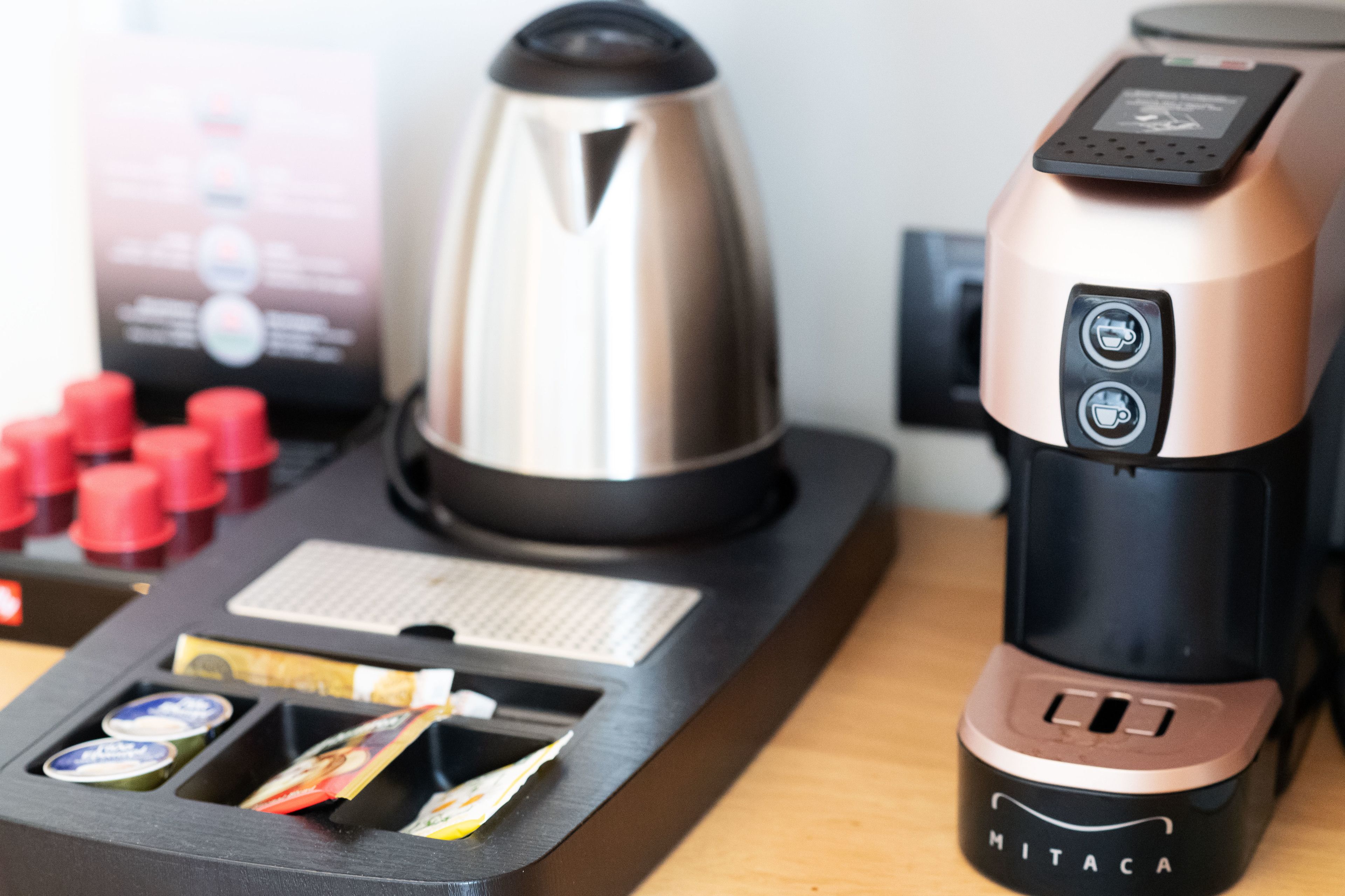 A coffee machine with a digital interface, a kettle, and a coffee pod holder on a wooden surface.